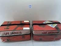Two rectangular red-orange fabric packs labeled 'LIFE JACKETS', each containing 4 life vests inside.