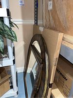 Two mirrors resting on floor against wall: round metal-framed mirror and rectangular metallic look mirror.