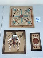 Three Native American art pieces on board including two wood-framed works and one unframed square board, showing overall lot arrangement