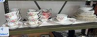 Full view of all items on shelf including stacked plates, cups and saucers, sugar bowl and platter.