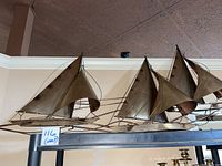 Full view of large metal wall hanging featuring three sailboats mounted on a wall shelf with ceiling in background.