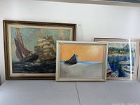 Photo of three framed seascape artworks showing clipper ships, a boat on sand, and sailboats in water.
