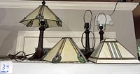 Three small table lamps with bronze bases and mission style stained glass shades. Two shades detached, one cracked.