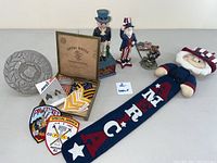 Overview photo of entire collection showing Veteran plaque, military patches and pins, two Uncle Sam cast iron mechanical banks, plush Uncle Sam figure, and fabric Americana banner.