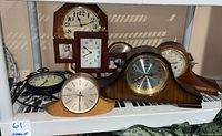 Shelf photo showing multiple vintage clocks including square photo frame clock, mantle clocks and round wall clock.
