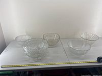 Four vintage clear glass punch bowls arranged on a table showing varying sizes and patterns.