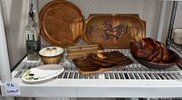 Photo showing the full assortment of wooden trays and bowls including the colorful bird-design tray, glass bottle and ceramic dishes.