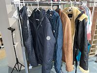 Rack of six women's jackets and coats hanging, showing various styles including leather and nylon with fur trim and belts