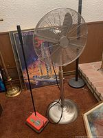 Side and front view of the Airworks metal floor fan beside the red electrostatic carpet sweeper on brown carpet.