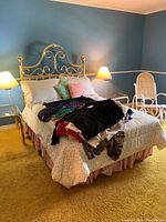 Full view of bed with gold-tone brass headboard, linens, and pillows in a bedroom with blue walls and yellow carpet. Clothing on bed not included.
