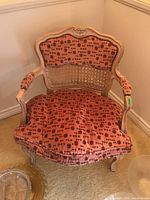 Front view of Bergere style chair showing pink floral upholstery, cane back, carved wooden frame, arms and carved legs.