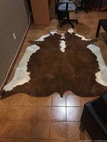 Top view of brown and white cowhide rug laid flat on tile floor showing natural irregular shape and color pattern.