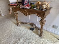 Side view of the ornately carved wood frame hall table with decorative glass top, showing details on legs and apron with ornate floral and scroll designs.