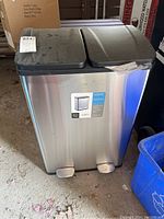 Front view of double step garbage can showing stainless steel body and black lids with label.