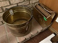 Wide shot of the brass bucket and magazine rack side by side on a brick hearth.