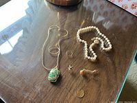 Overview of all four pieces on a glass tabletop: ring, pearl necklace, chain with pendant, brooch