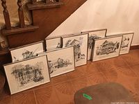 Eight metal framed black and white prints arranged leaning against a wall, showing various architectural scenes.