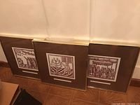 Three metal framed Judaic prints leaning against a wall, showing three different scenes.