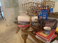 Full view of the table showing brass menorah, disposable candle holders, books, cup and plate.