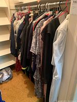 View of assorted ladies jackets, skirts, and dresses hanging on a closet rod showing varied colors and styles including dark and light clothing, some with patterns and some solid.