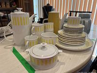 Full lot arrangement showing coffee pot, cups, saucers, creamer, sugar bowl, and plates on a table with consistent yellow striped pattern on white ceramic.