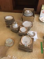 Overall view of dinnerware set stacked on carpet with pieces in cardboard boxes
