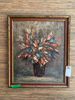 Full view of framed canvas painting depicting an abstract bouquet with a dark vase, featuring prominent orange and blue leaves, set against a textured gray background.