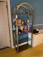 Front and angled side view of shelving unit with five smoked glass shelves and metal frame with arched top, showing wear and contents removed.