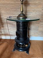 Full view of the space heater side table showing black metal heater base, glass top, and brass lamp base.