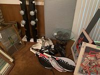 Full view of lot showing dumbbell stand with weights, Wilson tennis racquets in covers, white ladies' ice skates, and black sports helmets grouped on the floor.