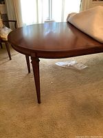 Full view of oval mahogany dining table surface and leg detail under natural light, showing polished wood and wear.