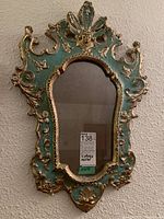 Front view of ornate teal and gold wall mirror with label indicating 26 x 18 dimensions