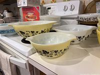 Three yellow Pyrex mixing bowls with black botanical pattern nested on countertop and stovetop. Bowls have spouted rims and show wear.