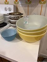 Set of four Pyrex mixing bowls including three yellow nested bowls and one blue bowl, placed on countertop near stove