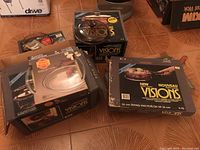 Photo showing boxed Visions cookware including a covered saucepan and frying pans on a tile floor