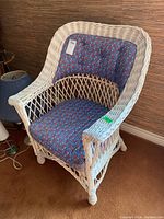 White wicker chair with blue floral patterned seat and back cushions, showing tufted button details and woven wicker construction.