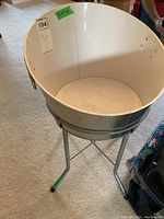 Front angle view of large round metal can cooler with white interior and attached gray metal stand with three legs.