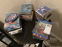 Photo of various CD and DVD cases on a black table showing game, music CDs, and movies