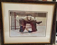 Framed and matted print showing the full artwork of a hockey goalie in a crouched position in front of the net, captured at an angle to show frame and matting.