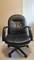 Front view of black leather office chair showing cushioned seat and backrest with armrests and caster wheels.