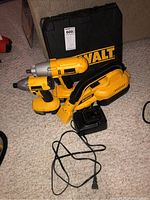 Photo shows DeWalt 18V cordless impact driver, impact wrench and cordless vacuum, with batteries and charger on carpeted floor, all in yellow and black.