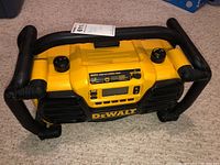 Front and side view showing the rugged frame and overall condition of the DeWalt DC012 work site radio and charger on carpeted floor.
