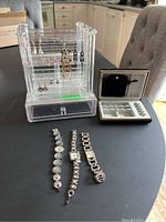 Full view of jewelry stand containing earrings, travel case, and three bracelets placed on table.