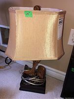 Front view of hockey-themed table lamp with beige fabric shade and miniature hockey equipment on base.