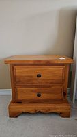 Side view of wood night stand showing two drawers and round black knob handles, wood has scratches.