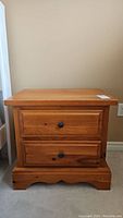 Front view of wood night stand showing two drawers with black knobs and overall condition.