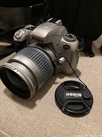 Silver Nikon F55 with attached 28-80mm lens and lens cap beside camera showing brand and model.