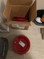 Red ceramic dinner plates inside cardboard box and one plate displayed outside with a sale sticker visible.