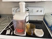 Front angle view showing the juicer body with transparent red juice container inside and included components beside it.