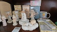 Image showing multiple Precious Moments porcelain figurines on a shelf including wedding couple, baby on cloud, graduates, lamb girl and others with several original boxes behind.